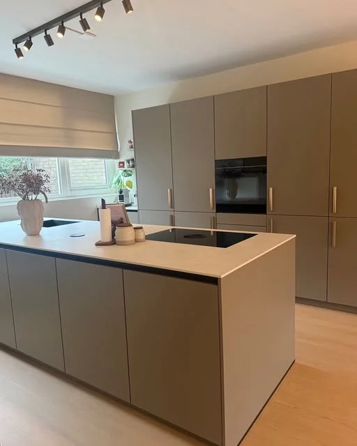 Keuken in warm grijs met een kookeiland, een plant en lichte houten vloer